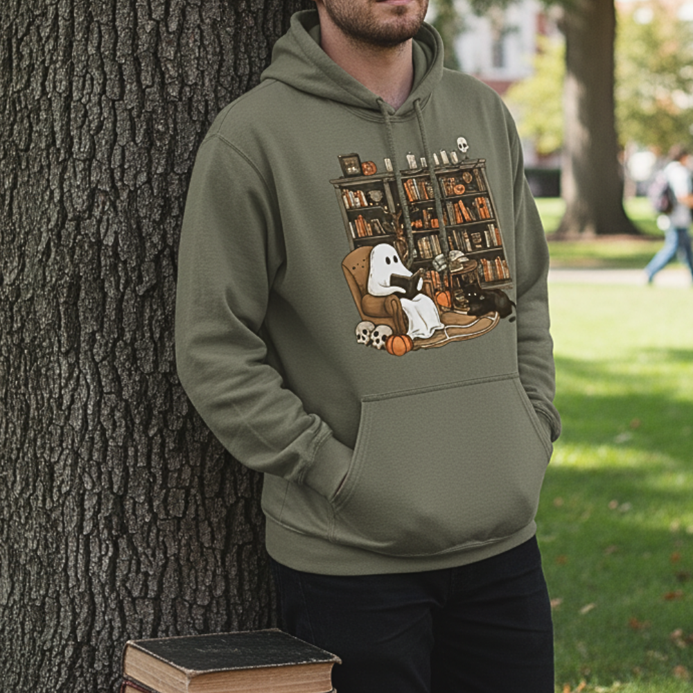 Person wearing a military green-colored hoodie with a graphic design of a ghost and dog in a library, standing next to a tree outdoors.