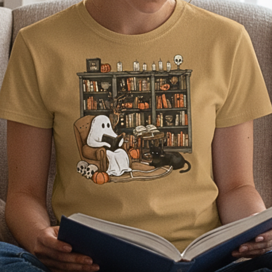 Person wearing a gold-yellow t-shirt with a cute ghost reading a book design, holding an open book in her lap.
